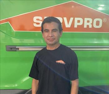 Male employee with black hair smiling in front of a green background