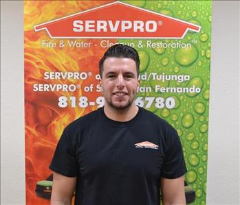 Male employee with black hair smiling in front of a green background