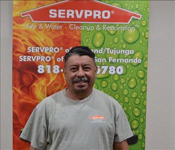 Male employee with black hair smiling in front of a green background