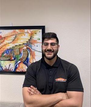 Male employee with black hair smiling in front of a tan background